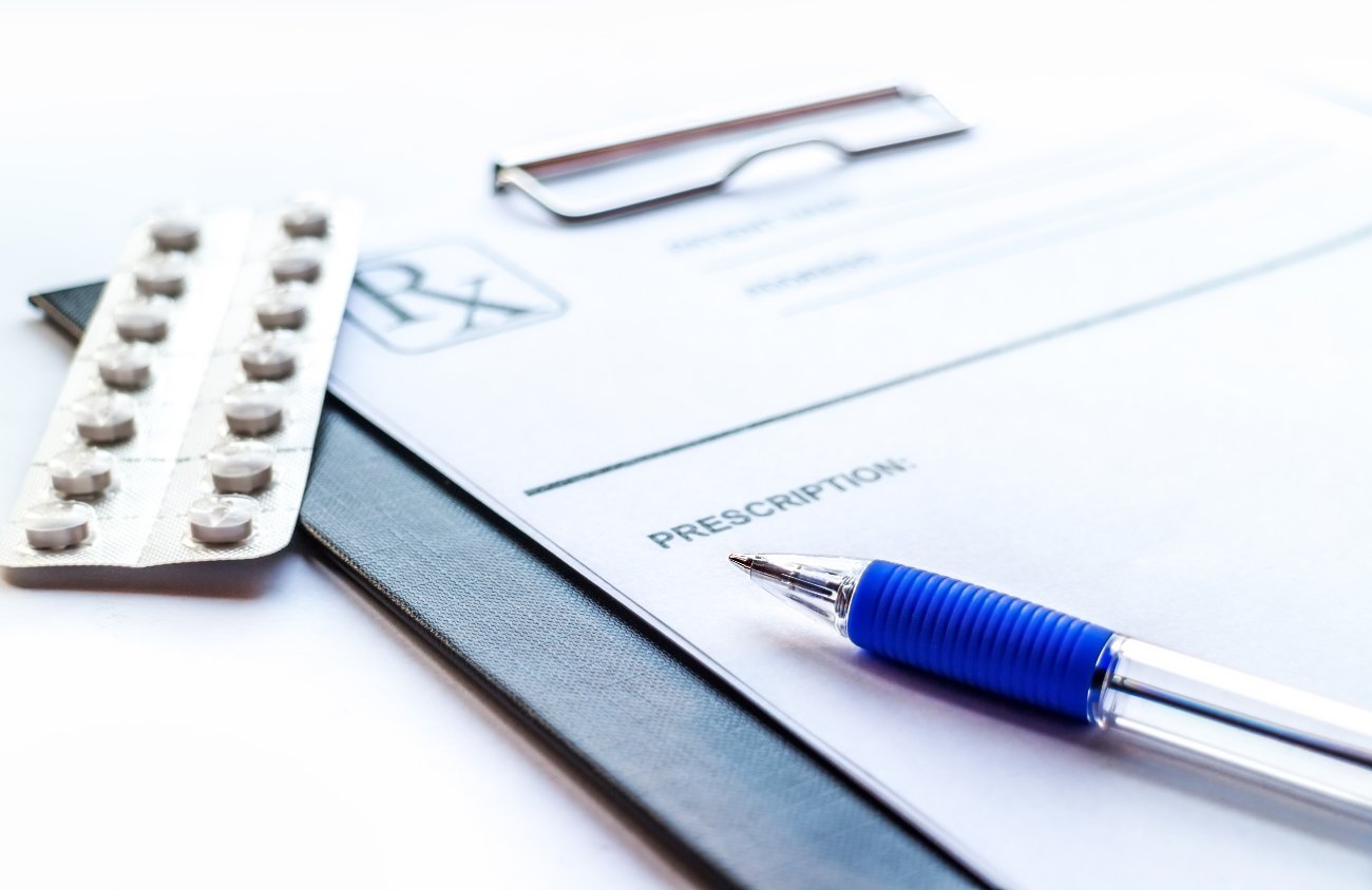 Pöydällä tyhjä resepti, kynä ja lääkeliuska.